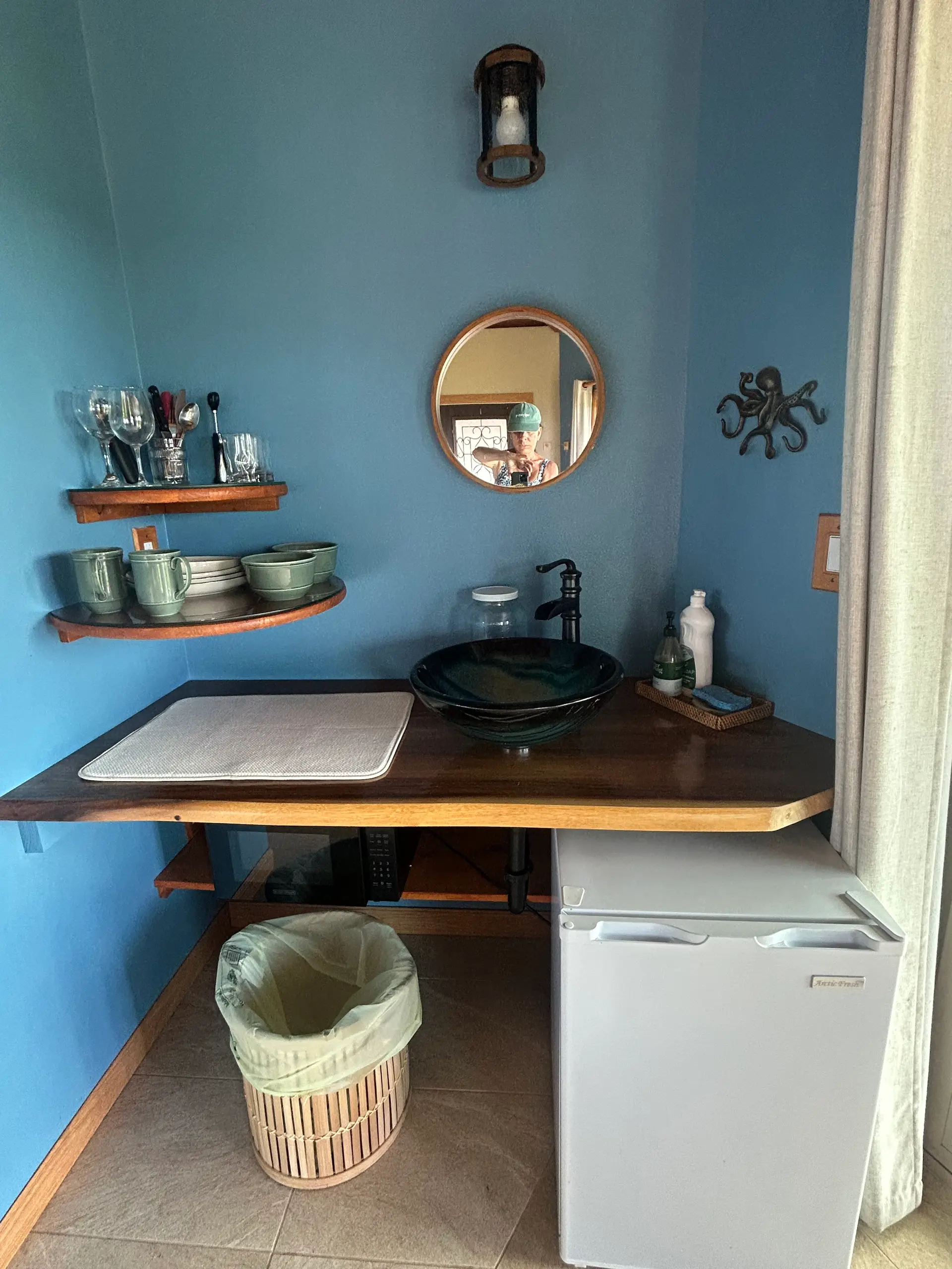 Blue kitchenette nook with a vessel sink, shelves, and mini fridge