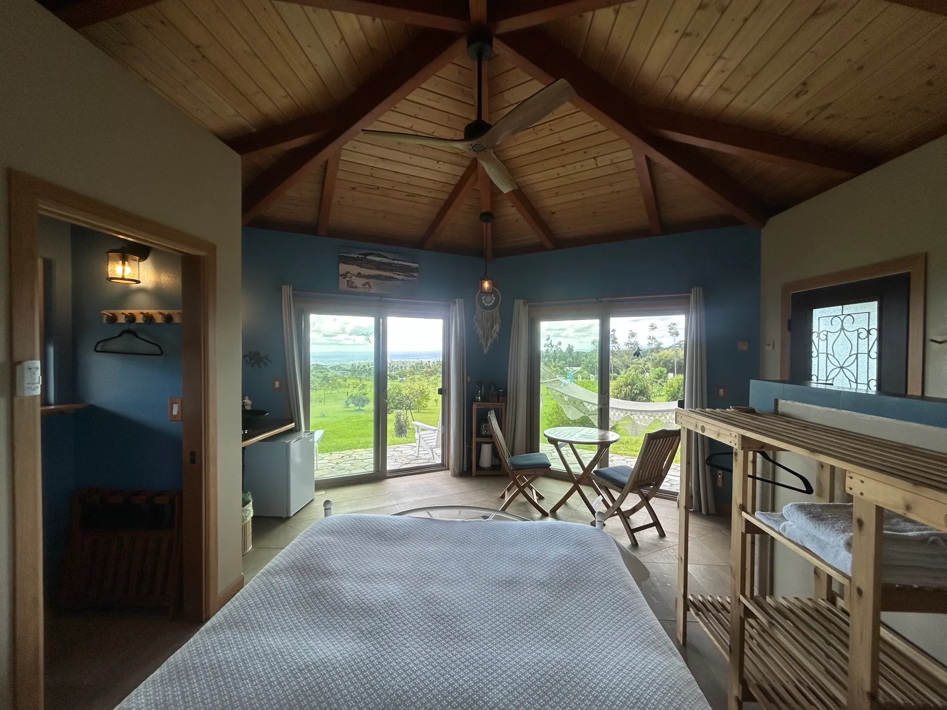Off-grid bungalow bedroom with a vaulted wood ceiling and sliding doors opening to pasture and ocean views